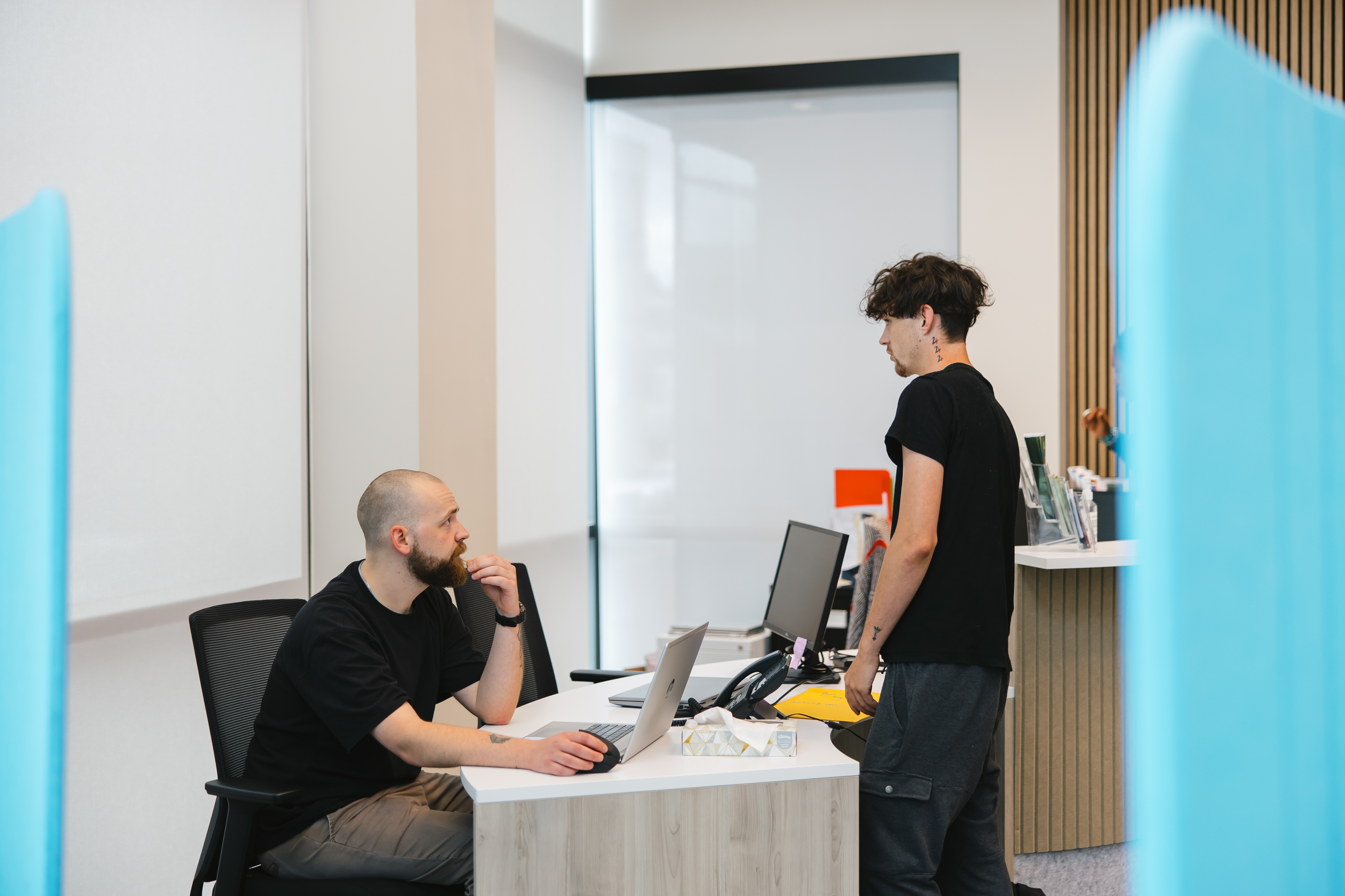 Young person standing at a desk asking a person sitting behind the desk a question.
