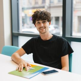 Youth smiling while sitting at a table, with a folder on the table.